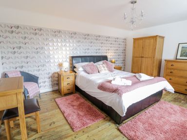 A bedroom with a bed a wooden wardrobe two bedside tables a wooden dresser a chair and pink rugs at Tai Ucha in Cerrigydrudion