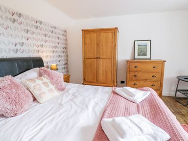 A bedroom with a bed with pink pillows and folded towels on a pink blanket wooden wardrobe and chest of drawers with a framed picture on top at Tai Ucha in Cerrigydrudion