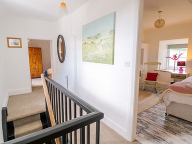 A hallway with stairs leading down two bedrooms visible one with a wooden wardrobe and the other with a rocking chair bedside table and bed at Tai Ucha in Cerrigydrudion