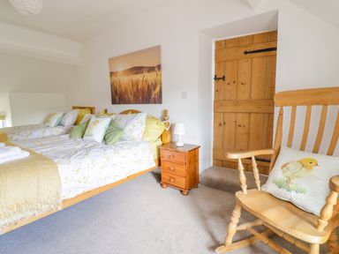 A bedroom with two single beds a wooden rocker chair with a chick pillow and a wooden door at Tai Ucha in Cerrigydrudion