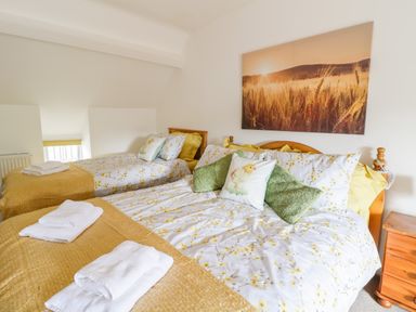 A bedroom with two beds with yellow and floral bedding and a sunset field picture on the wall at Tai Ucha in Cerrigydrudion