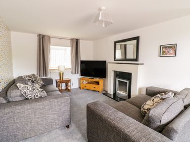 A living room with two grey sofas a television on a wooden stand a fireplace and a window with curtains at Tai Ucha in Cerrigydrudion