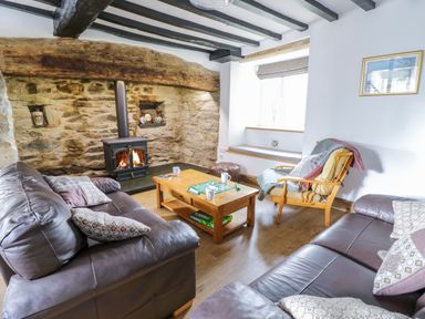 A living room with two leather sofas a wood stove and a wooden coffee table with a game at Tai Ucha in Cerrigydrudion