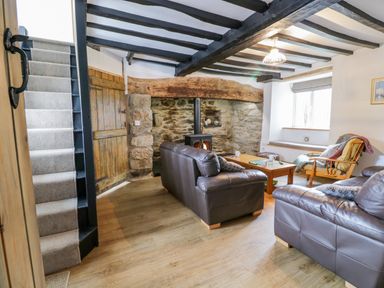 A living room with two leather sofas a coffee table a rocking chair a stone fireplace and stairs at Tai Ucha in Cerrigydrudion
