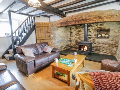 A living room with brown leather sofas a wooden coffee table with a board game and mugs a wood burning stove in a stone wall at Tai Ucha in Cerrigydrudion