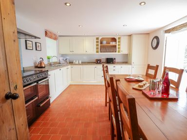 A kitchen with wooden dining table and chairs and white cabinets at Tai Ucha in Cerrigydrudion