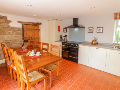 A kitchen with wooden dining table and chairs a black stove and white cabinets at Tai Ucha in Cerrigydrudion