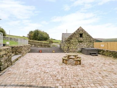 An outdoor patio area with stone walls a wooden round picnic table and a hot tub at Tai Ucha in Cerrigydrudion