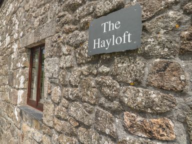 A stone exterior wall with a small window and a sign that reads The Hayloft at The Hayloft St Neot near Dobwalls