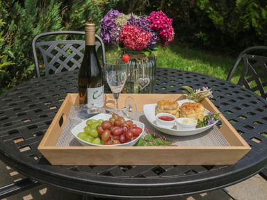 A wooden tray on a black metal table with a wine bottle two glasses a bowl of grapes a plate of scones with cream and jam and a vase of flowers at The Hayloft in St Neot near Dobwalls