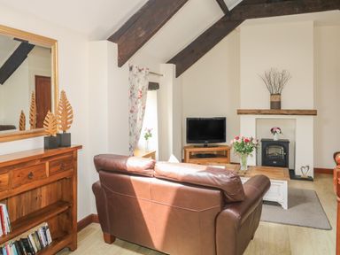 A living room with a brown leather sofa a wooden cabinet a television and flowers on a table at The Hayloft in St Neot near Dobwalls