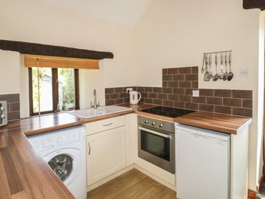 A kitchen with a washing machine sink oven refrigerator and hanging utensils at The Hayloft in St Neot near Dobwalls