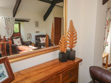 A living room with wooden furniture leather chairs and decorative leaves in front of a mirror at The Hayloft in St Neot near Dobwalls
