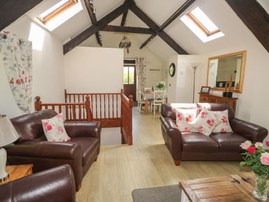 A living room with brown leather sofas floral cushions wooden stair railing dining table and skylights at The Hayloft St Neot near Dobwalls