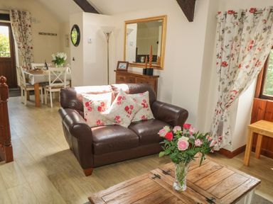 A living room with a brown leather sofa with floral cushions and a wooden coffee table with flowers at The Hayloft in St Neot near Dobwalls