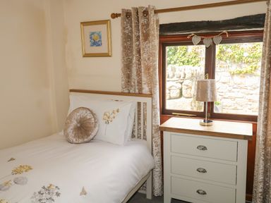 A bedroom with a bed with floral bedding a dresser with a lamp and a window with curtains at The Hayloft in St Neot near Dobwalls