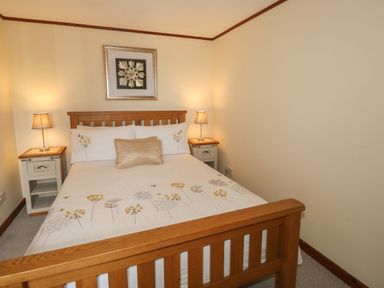 A bedroom with a wooden bed frame two bedside tables with lamps and a framed picture above the bed at The Hayloft in St Neot near Dobwalls