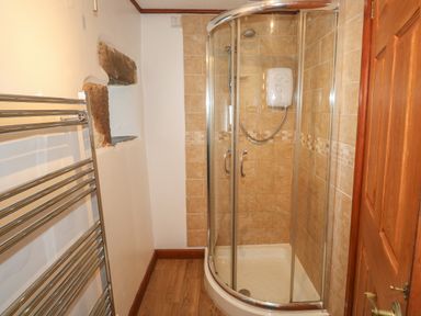 A bathroom with a corner shower enclosure with glass doors a chrome towel rack and wooden door at The Hayloft in St Neot near Dobwalls