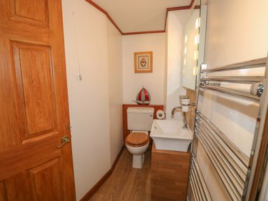 A small bathroom with a wooden door a toilet with a wooden seat a white sink and a metal towel warmer at The Hayloft in St Neot near Dobwalls