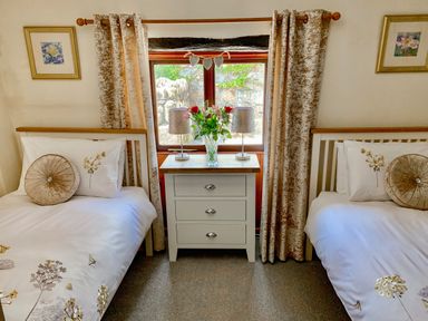A bedroom with two single beds a white nightstand with lamps and flowers between them at The Hayloft in St Neot near Dobwalls