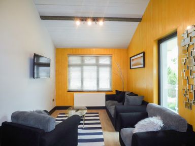A living room with two black and gray sofas a glass coffee table a striped rug a wall-mounted television and a window with blinds at Hidden Gem Cabin in Lettermacaward near Dungloe County Donegal