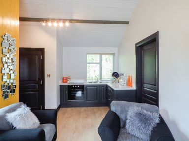 A small kitchen with black cabinets and orange pots near two black sofas with gray cushions at Hidden Gem Cabin in Lettermacaward near Dungloe County Donegal