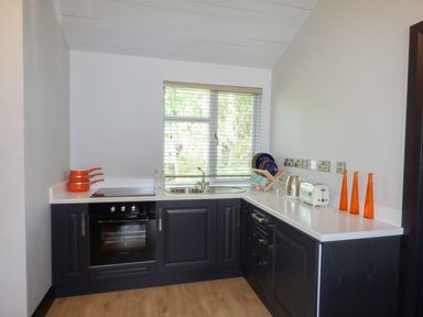 A kitchen with black cabinets white countertops a sink an oven toasters and orange vases at Hidden Gem Cabin in Lettermacaward near Dungloe County Donegal
