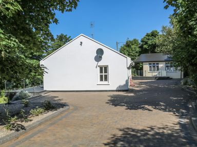 A paved driveway with a white house and a small building surrounded by trees at Hidden Gem Cabin in Lettermacaward near Dungloe County Donegal