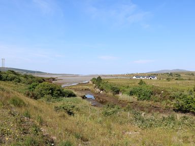 A rural landscape with grassy fields bushes a small stream and houses in the distance at Hidden Gem Cabin in Lettermacaward near Dungloe County Donegal