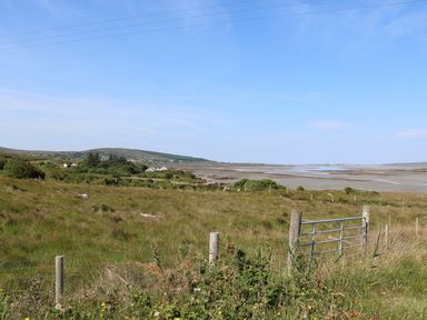 A grassy field with a metal gate near a coastline and hills in the background at Hidden Gem Cabin in Lettermacaward near Dungloe County Donegal