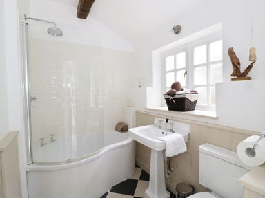 A bathroom with a curved bathtub and shower screen a pedestal sink a toilet and a window with a basket of towels at Blenheim Edge The Causeway in Woodstock