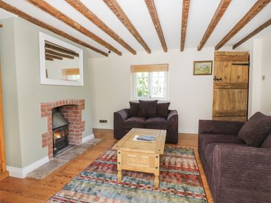 A living room with exposed wooden beams two dark sofas a wooden coffee table a brick fireplace a window and a wooden door at Blenheim Edge The Causeway in Woodstock