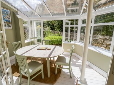 A dining area with a round table and four chairs in a glass conservatory at Blenheim Edge The Causeway Woodstock