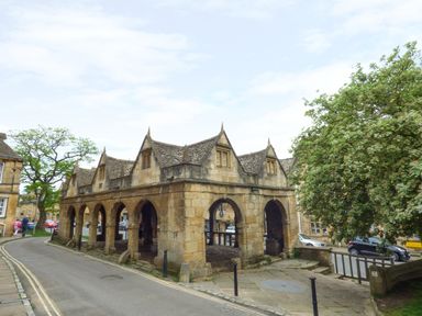 A stone market hall with pointed roof structures next to a tree and road at Blenheim Edge The Causeway in Woodstock