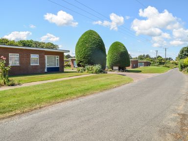 A road with grass lawns and hedges beside brick houses at 21 Siesta Mar in Mundesley