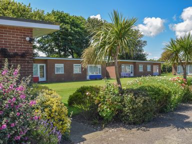 A garden with bushes and flowers in front of brick bungalows at 21 Siesta Mar in Mundesley