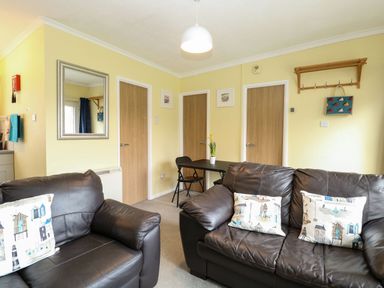 A living room with two brown leather sofas a small black table with two chairs and three wooden doors at 21 Siesta Mar in Mundesley