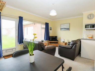 A living room with black sofas TV and yellow flowers on a table at 21 Siesta Mar in Mundesley