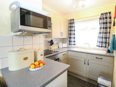 A kitchen with a microwave oven on a wall bracket and a bowl of fruit on the counter at 21 Siesta Mar in Mundesley
