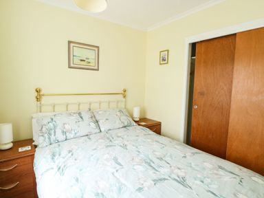 A bedroom with a floral bedspread two wooden bedside tables and framed pictures on the wall at 21 Siesta Mar in Mundesley