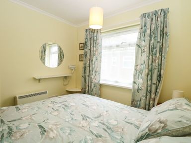A bedroom with a bed covered in floral bedding a window with matching curtains a circular mirror and a wall-mounted hairdryer at 21 Siesta Mar in Mundesley