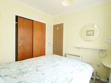 A bedroom with a bed floral bedspread wooden wardrobe doors a wall mirror and a door at 21 Siesta Mar in Mundesley