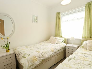 A bedroom with two single beds and a window with green curtains at 21 Siesta Mar in Mundesley