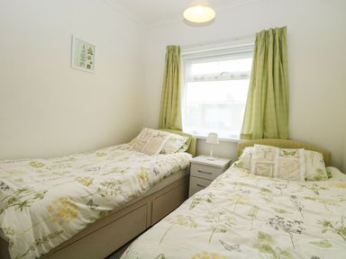 A bedroom with two single beds a small white nightstand with a lamp and green curtains at 21 Siesta Mar in Mundesley
