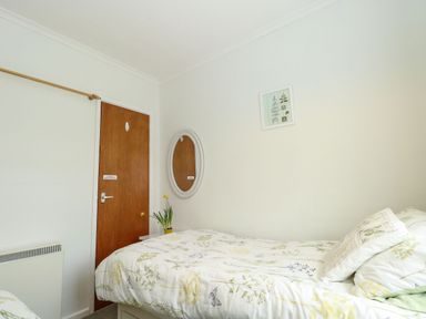 A bedroom with a single bed next to a brown wooden door with a round mirror on the wall and a small plant on a nightstand at 21 Siesta Mar in Mundesley