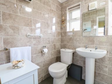 A bathroom with a toilet a pedestal sink a mirror a towel rack and a small cabinet at 21 Siesta Mar in Mundesley