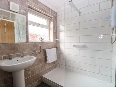 A bathroom with a pedestal sink a mirror a window and a shower area at 21 Siesta Mar in Mundesley