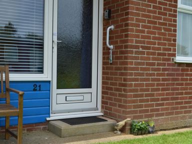 A front door with a porch step a wooden bench to the left and plants and a duck statue to the right at 21 Siesta Mar in Mundesley