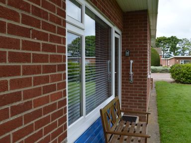 A wooden bench outside a brick house with a window and a door surrounded by grass at 21 Siesta Mar in Mundesley