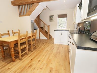 A kitchen with white cabinets wooden dining table and chairs and wooden stairs at The Coach House in Llanrwst